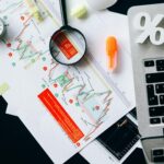 Top view of financial documents, charts, and laptop organized on a desk.