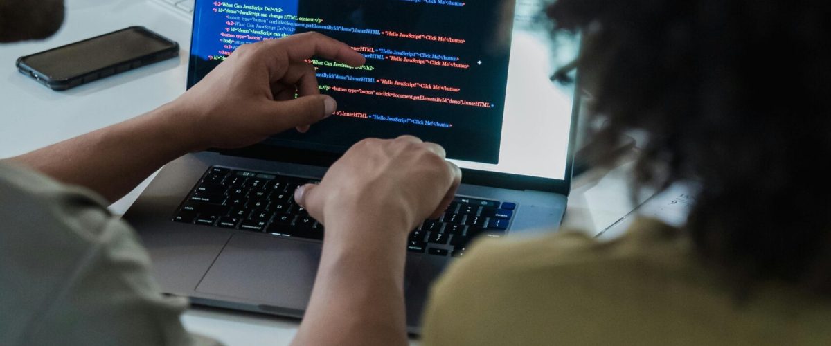 Two adults collaborating on programming tasks using a laptop in an office setting.